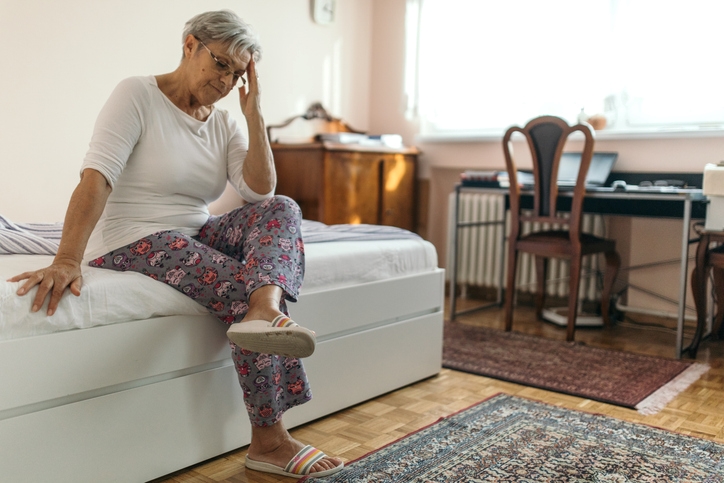 Woman sitting on a bed with her hand on her head
