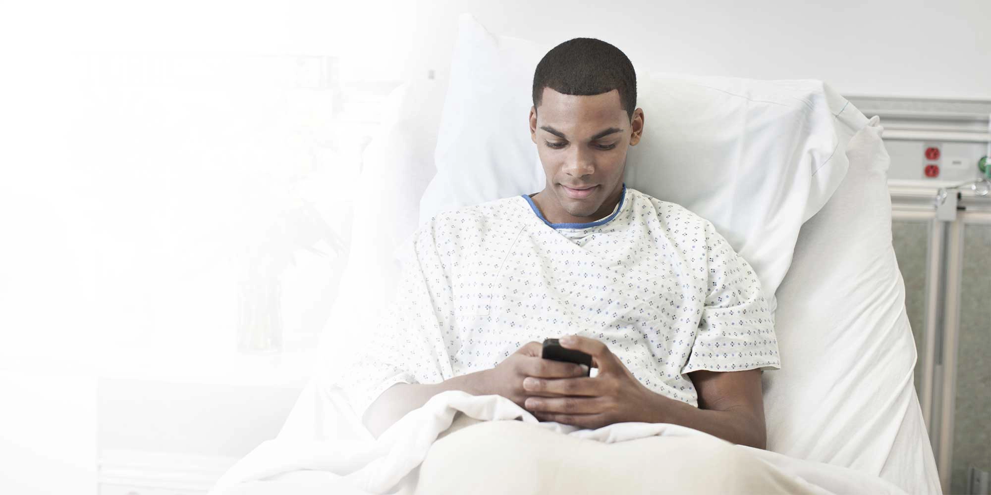A young man sits in a hospital bed using his phone