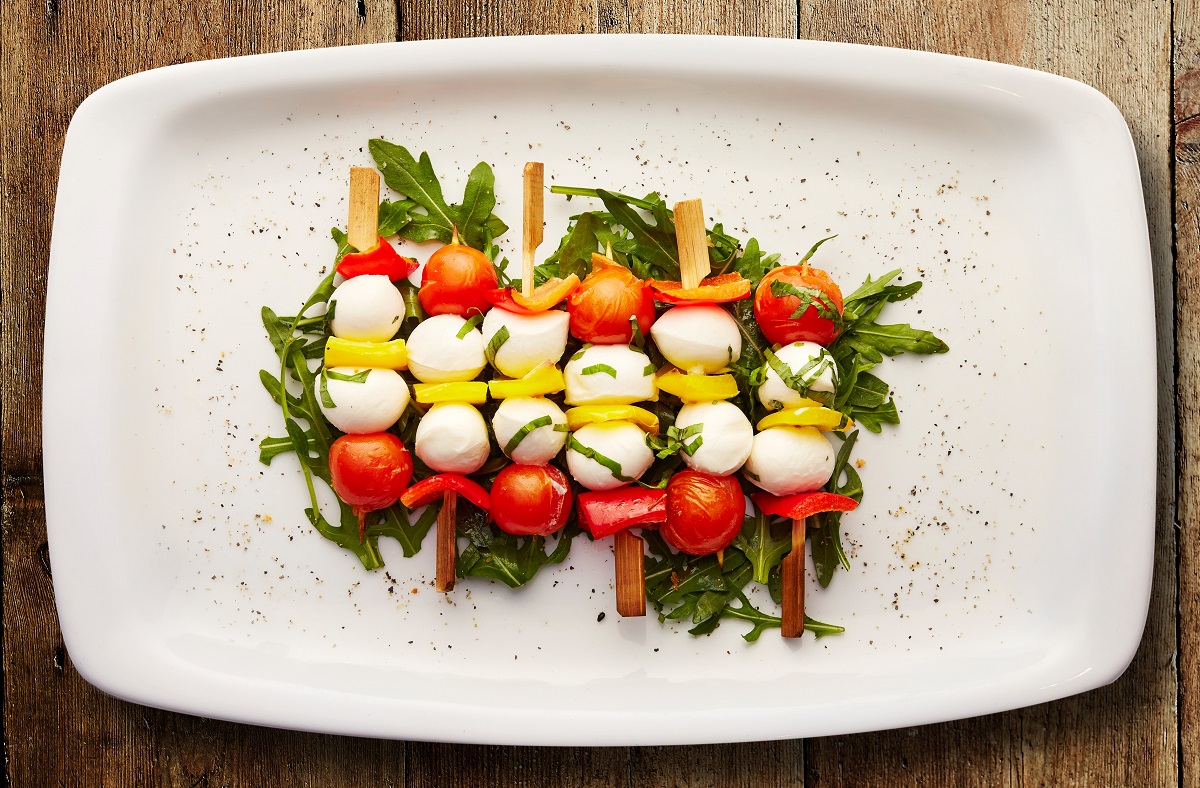 Cheese, tomato, and yellow bell pepper slices skewers on top of a bed of spinach on a white plate.