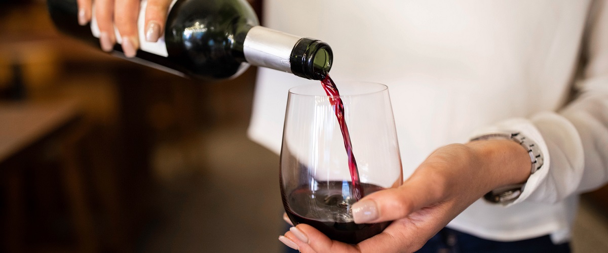 Caucasian female hands holding a green wine bottle and pouring red wine into a wine glass she is holding.
