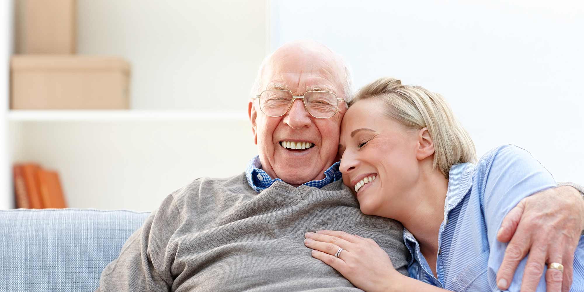 A senior man and his daughter share a sweet moment laughing together in the comfort of their home