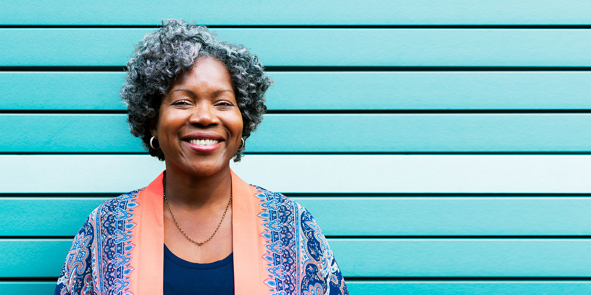 A beautiful older woman stands in front of a blue wood wall